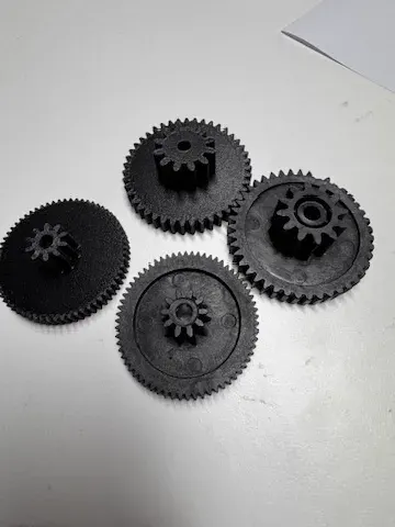Quatre engrenages noirs imprimés en 3D, posés à plat, pièces de remplacement