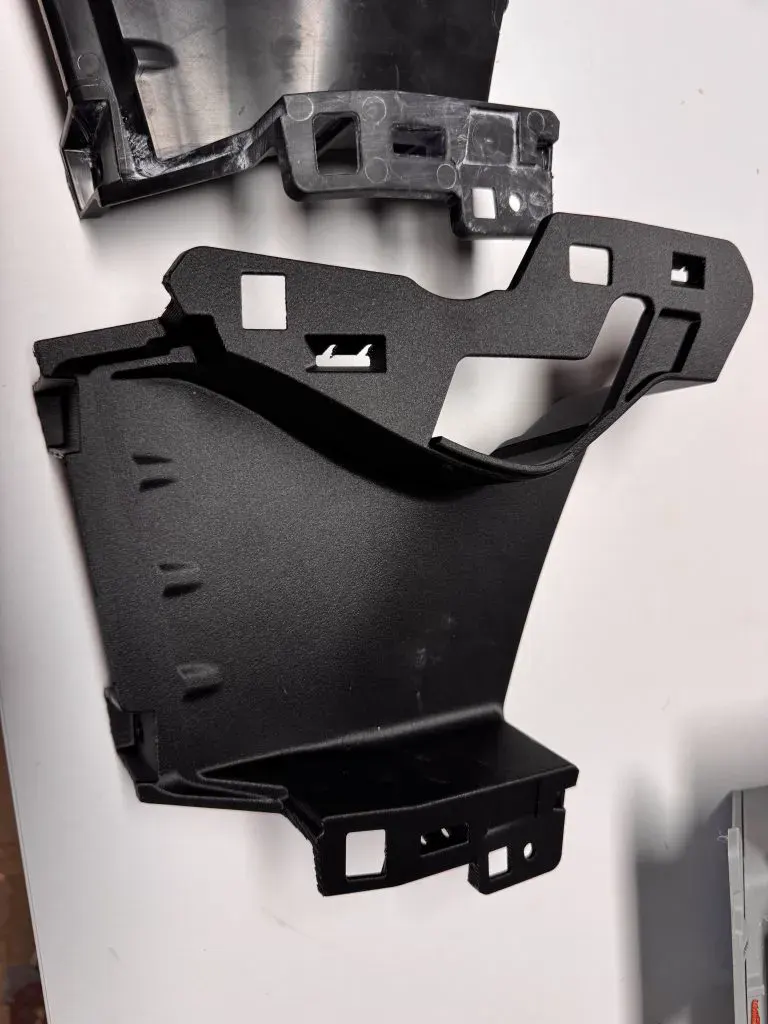 Pièce technique noire de carrosserie automobile imprimée en 3D, avec ses pattes de fixation et ses ouvertures