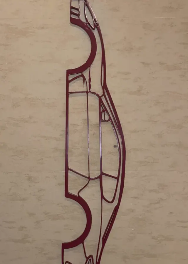 Silhouette filaire d'une voiture de sport, imprimée en 3D en rouge foncé, fixée sur un mur en bois clair